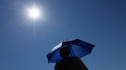 Eine Frau läuft mit Sonnenschirm unter der strahlenden Sonne.