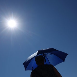 Eine Frau läuft mit Sonnenschirm unter der strahlenden Sonne.