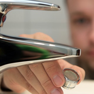 Mann vor Wasserhahn, hat Perlstrahler-Aufsatz in der Hand