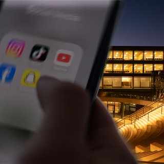 Ein Smartphone mit Social Media App Icons, vor dem Landtag in Stuttgart bei Nacht.