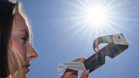 Eine junge Frau setzt sich eine Sonnenfinsternisbrille auf.