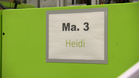 Eine grüne Metallwand mit der Aufschrift Maschine 3 und dem Vornamen Heide. Die Freiburger Firma Glassomer stellt mit dieser Maschine ganz besonderes Glas her. Laut eigener Aussage weltweit einmalig.