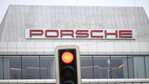 Eine rote Ampel leuchtet vor einem Gebäude mit dem Porsche-Schriftzug.
