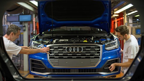 Fertigungsmechaniker bringen an einem Fließband im Audi-Werk die Front an einem Audi an.
