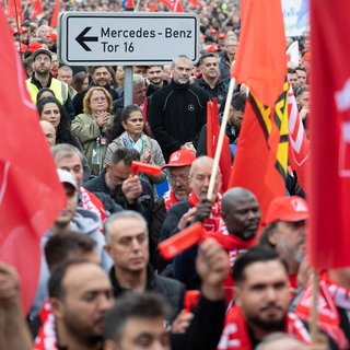 Mitarbeitende der Mercedes-Benz AG stehen während einer Aktion der IG Metall auf einer Zufahrt zum Mercedes-Benz Werk.