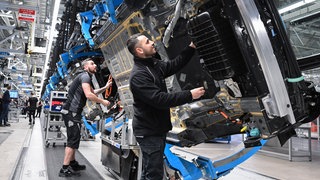 Mitarbeiter von Mercedes-Benz arbeiten in der Fertigung am Band. 