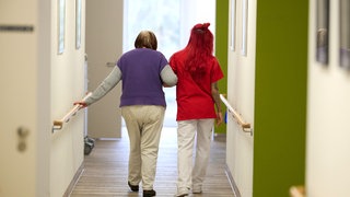 Eine Pflegekraft begleitet in einem Pflegezentrum eine Seniorin durch den Flur.