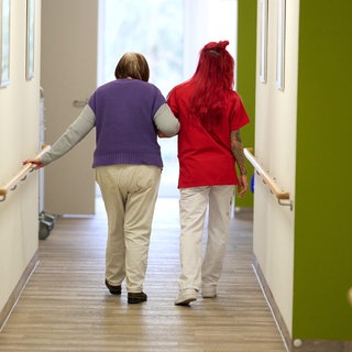 Eine Pflegekraft begleitet in einem Pflegezentrum eine Seniorin durch den Flur.