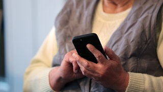 Eine alte Frau tippt auf ihrem Handy.