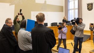 Der Angeklagte verbirgt sein Gesicht hinter einem Aktenordner in einem Verhandlungssaal im Landgericht Gießen.