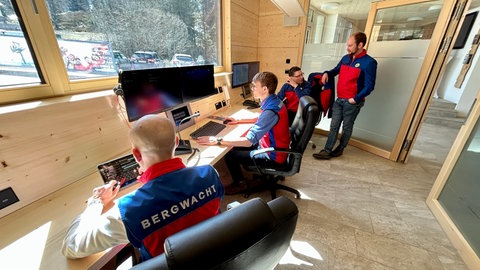 In der neuen Bergwacht arbeiten die Retter in ihrer rot-blauen Einsatzkleidung. Modernste Technik (Monitore, Einsatzfahrzeuge) unterstützen sie.