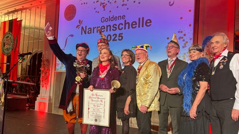 Regina Halmich mit Goldener Narrenschelle und Urkunde im pinken Glitzerkostüm, unter anderem umgeben vom Präsidenten der VSAN und Innenminister Thomas Strobl
