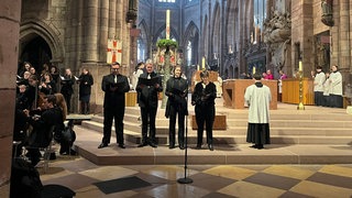 Sängerinnen und Sänger stehen neben dem Altar im Freiburger Münster. Sie tragen schwarz.