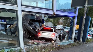 Ein weißes Auto hat bei einem Unfall die Scheibe eines Autohauses durchbrochen.