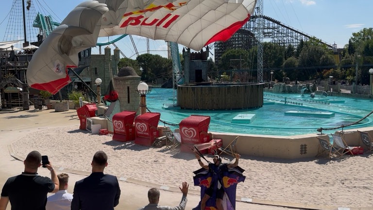Ein Extremsportler landet mit einem Wingsuit vor einer Achterbahn im Europapark.