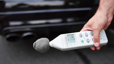 Symbolfoto: Ein Polizeibeamter misst in Mannheim  bei der Kontrolle von Auto-Tunern die Lautstärke des Auspuffs. In Freiburg hat die Polizei ein zu stark getuntes Auto aus dem Verkehr gezogen.