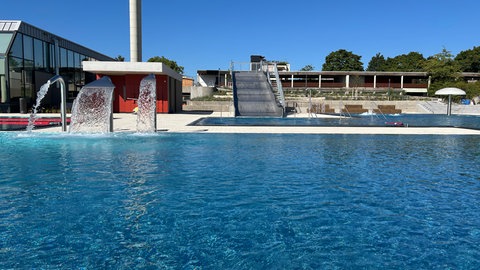 Die spezielle Form des Beckens trennt den Spaß- vom Schwimmbereich. Im Hintergrund ist die Rutsche zu sehen.