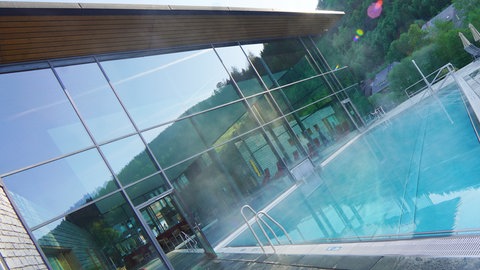 Der Außenbereich eines Schwimmbades, aus dem Becken steigt Dampf auf.
