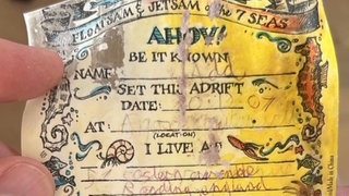 Eine vergilbte Nachricht mit unleserlicher Schrift und Meerestieren an den Rändern ist zu erkennen. 