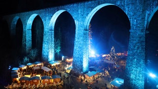 Farbenspiel am Viadukt beim Weihnachtsmarkt, darunter tummeln sich die Besucher an den zahlreichen Hütten und Buden.