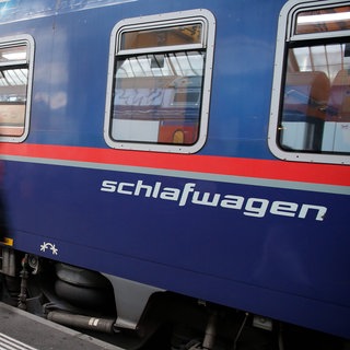 Ein Reisender mit einem Rucksack läuft vor einem Nachtzugwagen vorbei, auf dem das Wort Schlafwagen steht