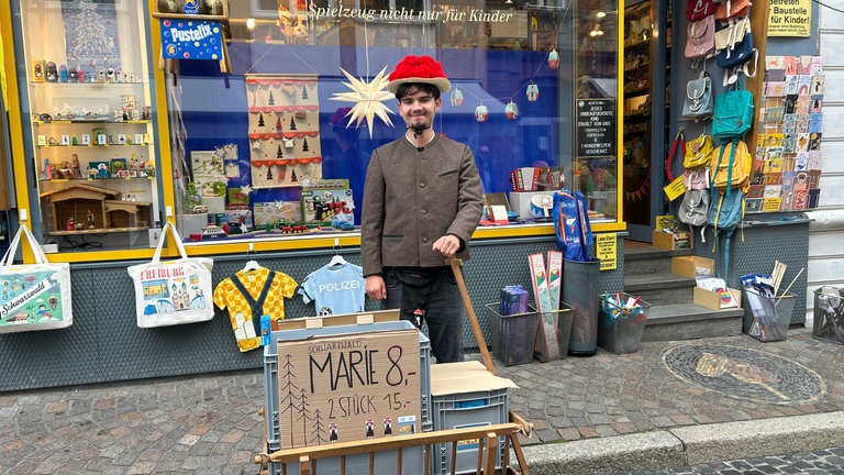 Ein junger Mann läuft mit Bollenhut und Bollerwagen durch Freiburg, um die Playmobil-Figur "Schwarzwald Marie" auf der Sztaße zu verkaufen.