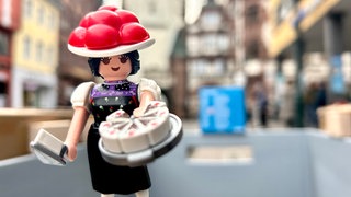 Die Playmbobilfugur "Schwarzwald Marie" mit Bollenhut, Tortenheber in der einen und eine Schwarzwälder Kirschtorte in der anderen Hand. 