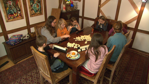 Pflegefamilie mit sechs Kindern sitzt am Tisch und spielt ein Brettspiel.