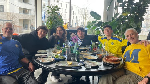 Fans von Maccabi Tel Aviv sitzen teilweise in Trikots in einem israelischen Restaurant in Freiburg um einen Tisch. 