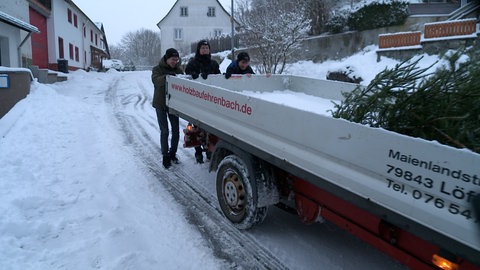 Drei Zwanzger halten sich am Ende des Pick-ups fest und rutschen den Berg runter. 