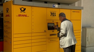 Ein Mann steht vor einer gelben Poststation.
