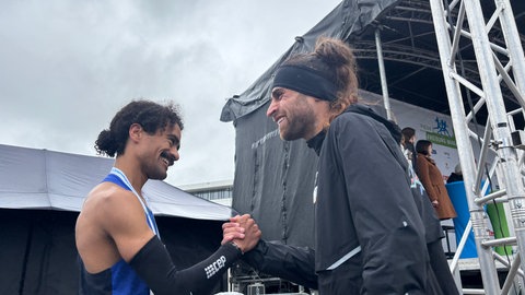 Marathon-Gewinner Omar Tareq (rechts) und Halbmarathon-Gewinner Enoque Buchegger (links) geben sich nach ihrem Lauf hinter der Ziellinie die Hand. 
