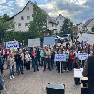 Menschen stehen bei einer Kundgebung und halten Schilder hoch. Wutacher:innen fordern Rücktritt ihres Bürgermeisters.