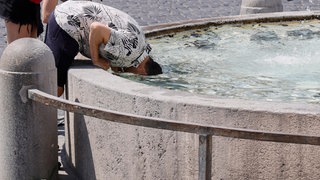Ein Mann steckt seinen Kopf in einen Brunnen, um sich abzukühlen. 