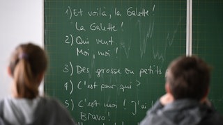 Zwei Schüler sitzen vor einer mit Inhalten aus dem Französischunterricht beschriebenen Tafel. Französisch wird an Schulen in BW immer unbeliebter: Die Fête de la Musique soll die Kinder und Jugendlichen wieder auf den Geschmack bringen.
