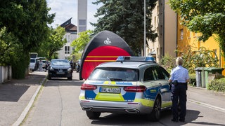Beamte der Kriminalpolizei und der Kriminaltechnik stehen in einem Offenburger Wohngebiet, während im Vordergrund ein Einsatzfahrzeug der Polizei steht.