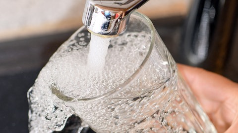 Ein Glas wird unter einem Wasserhahn befüllt. 