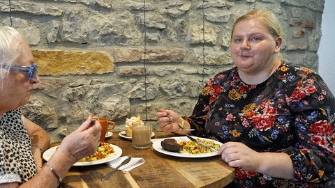 Zwei Frauen sitzen an einem Tisch und essen. 