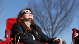 Eine Frau schaut nach oben und trägt eine Sonnenfinsternis-Brille. 