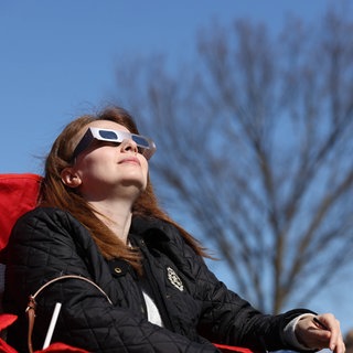 Eine Frau schaut nach oben und trägt eine Sonnenfinsternis-Brille. 