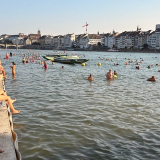 Mehrere Duzend Menschen sitzen am Rhein in Basel und beobachten den Ausstieg beim offiziellen Rheinschwimmen 2026.