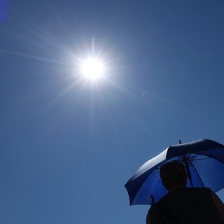 Eine Frau läuft mit Sonnenschirm unter der strahlenden Sonne.