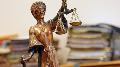 Justizia-Figur vor Aktenstapeln