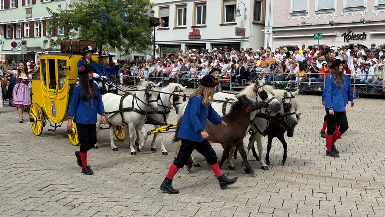 Eine gelbe Postkutsche wird beim historischen Umzug von Pferden durch die Altstadt von Biberach gezogen.