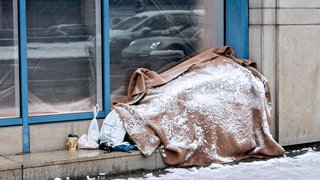 Schneebedeckter Schlafplatz eines Obdachlosen am Bürgersteig. Trotz Schnee und Eis suchen nicht alle Betroffenen Hilfe in Notunterkünften.