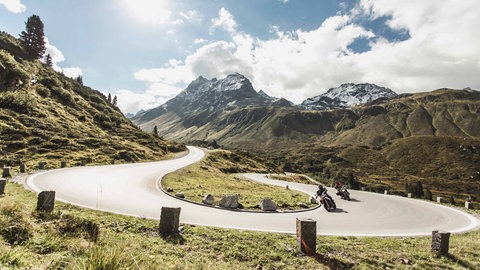 Zwei Motorräder fahren die Silvretta-Hochalpenstraße entlang. Im Hintergrund sind die Berge zu sehen.