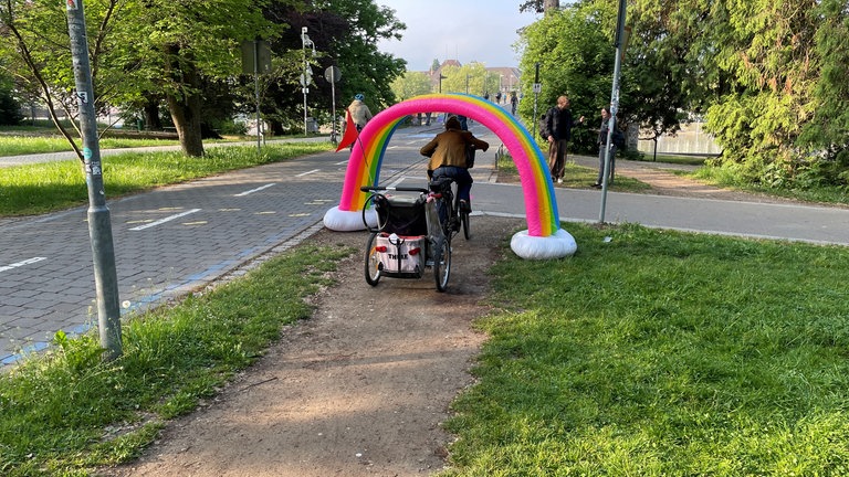 Ein Fahrradfahrer fährt durch einen großen aufgestellten Regenbogen. Die Katholische Kirchengemeinde Konstanz bietet am Freitagmorgen einen "Segen to go" für Radfahrerinnen und Radfahrer an.