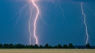 Mehrere Blitze zucken über einem Landstrich Richtung Boden. Nun wurde bei einem Blitzeinschlag in Aitrach (Kreis Ravensburg) eine Frau verletzt: beim Laden ihres Smartphones.