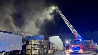 Die Feuerwehr löscht den Brand in einem Entsorgungsbetrieb in Friedrichshafen. Dabei hat sie eine Drehleiter im Einsatz.