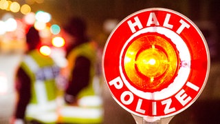  Ein Polizist hält bei einer Verkehrskontrolle eine rote Kelle mit der Aufschrift "Halt Polizei" hoch